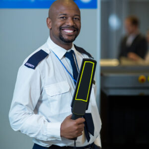 Portrait of smiling airport security officer holding metal detector in airport terminal